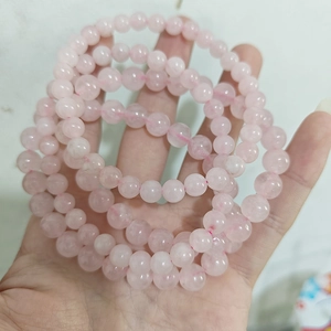 Macro shot of multiple light pink quartz bead bracelets held in hand showing smooth texture