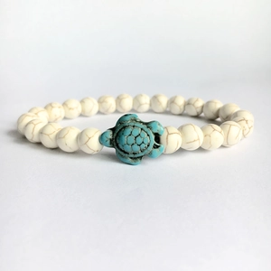 Detail of beaded bracelet featuring white turquoise stones and green turtle charm
