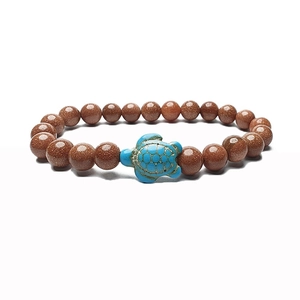 Macro shot of goldstone beaded bracelet featuring a blue turquoise turtle charm detail