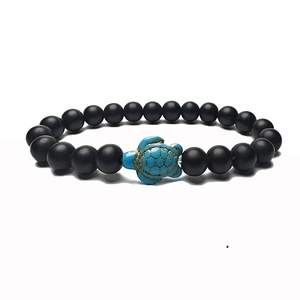 Macro detail of matte black beads bracelet with light blue sea turtle charm