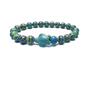 Macro shot of green turquoise beads and gold-detailed sea turtle charm on elastic bracelet
