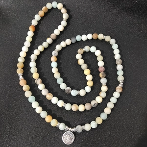 Detail view of 108 matte Amazonite beads with silver lotus flower pendant on black surface