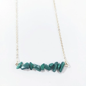 Macro detail of natural green irregular stone chips on a minimalist gold necklace