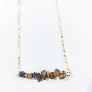 Macro detail of natural irregular tiger eye stones on a minimalist gold link chain necklace
