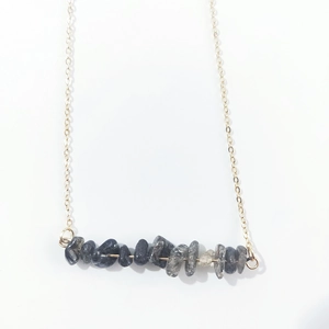 Detail view of irregular dark natural stones on a delicate gold chain necklace