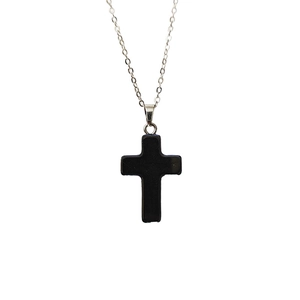 Détail macro du pendentif croix en pierre naturelle noire sculptée avec chaîne argentée