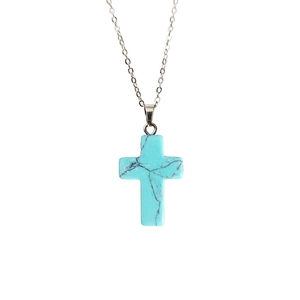 Détail d'un pendentif croix en turquoise avec veines noires sur une chaîne argentée