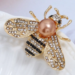 Macro shot of bee brooch with crystal wings and a large bronze pearl on a white texture