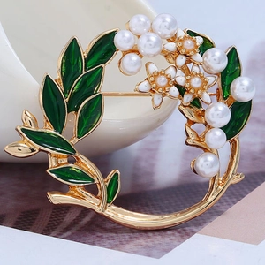 Details einer Blumenbrosche mit grünen Emailleblättern, weißen Perlen und Goldnadel
