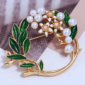 Detailaufnahme einer goldenen Kranz-Brosche mit grünen Blättern und Perlen