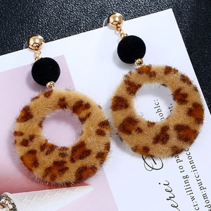 Close-up of leopard print plush hoop earrings with gold studs and black velvet balls