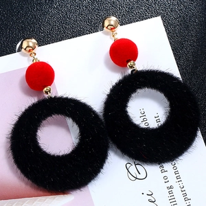Close-up of geometric plush drop earrings with red velvet ball and black fuzzy hoop