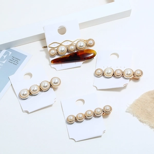 Lot de cinq barrettes dorées élégantes avec perles blanches et résine ambrée sur carte