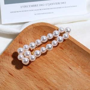 Vue macro d'une barrette dorée ajourée avec double rangée de perles sur bois