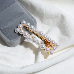 Détail d'une barrette rectangulaire dorée ornée de deux rangées de perles blanches