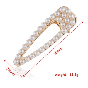 Détail d'une pince à cheveux dorée évidée avec perles blanches, dimensions 80 mm sur 25 mm