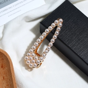 Détail macro d'une barrette triangle évidée élégante avec perles blanches sur base dorée