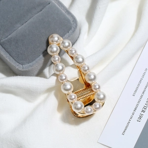 Détail de la pince à cheveux en perles dorées sur une boîte à bijoux en velours gris chic
