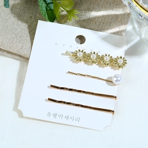 Élégant ensemble de quatre barrettes dorées avec perles et marguerites sur carte blanche