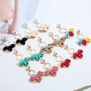 Detail of bohemian woven shell earrings set with pearls and straw base in vibrant colors