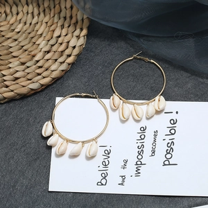 Detail of golden hoop earrings with white natural sea shells on a bohemian woven background