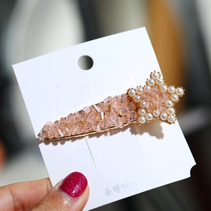 Detailed macro view of a pink crystal hair clip with pearl star accents on a display card