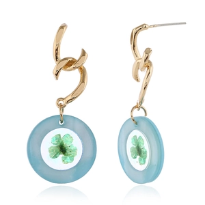 Detalle de pendientes dorados ondulados con resina azul claro y flor seca verde