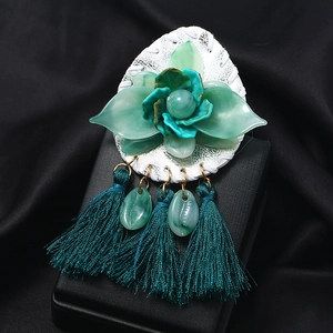 Green acrylic flower brooch with shell charms and silk tassels on a black jewelry box