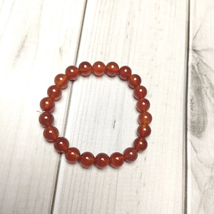 Macro shot of 8mm polished reddish-brown agate beaded bracelet on white wood