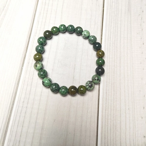 Top-down view of 8mm mottled green stone beads bracelet on white wood texture