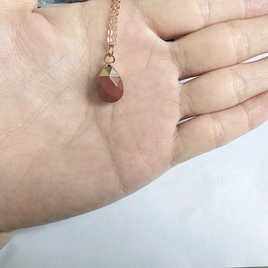 Close-up of teardrop shaped red goldstone pendant necklace held in hand