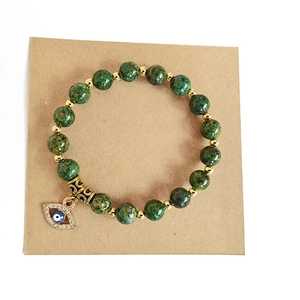 Detail von grünen Steinperlen Armband mit goldenem Evil Eye Anhänger auf Kraftkarte