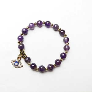 Detail eines Perlenarmbands mit Amethyststeinen und funkelndem Evil-Eye-Anhänger