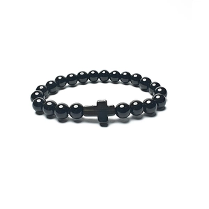 Close-up of polished black agate beads with a metallic cross charm on a beaded bracelet