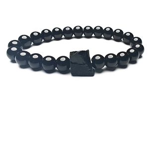 Primer plano de cuentas de piedra negra pulida y piedra bruta en pulsera elástica