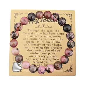 Pulsera de cuentas de rodonita natural con dije de corazón sobre tarjeta de regalo