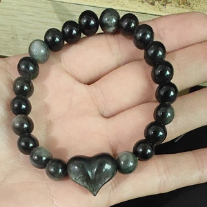 Bracelet en perles d'obsidienne argentée avec breloque cœur doré tenu dans la main