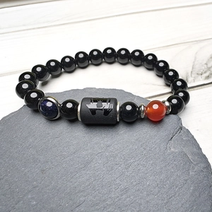 Dettaglio di un bracciale con perline nere e pietra blu sabbia su roccia grigio scuro