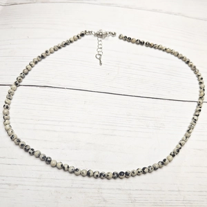 Detail of dalmatian jasper beaded necklace with silver lobster clasp on wood background