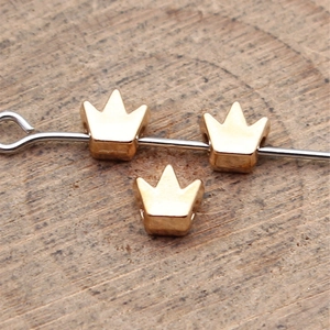 Golden crown spacer beads for DIY jewelry making displayed on a wooden surface