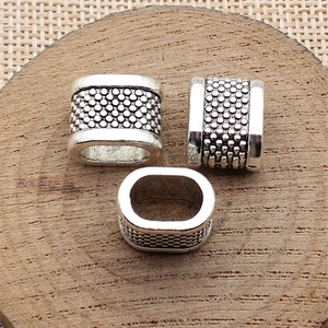 Three pieces of antique silver oval spacer beads with dot texture on wooden base