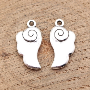 Pair of antique silver wing pendants made of zinc alloy on a natural wood surface