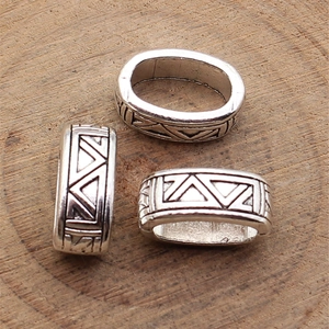 Antique silver oval beads with geometric triangle patterns on rustic wood background