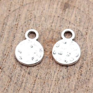 Pair of round hammered texture zinc alloy charms on natural wood grain background