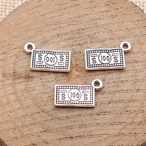Three antique silver dollar bill 100 dollar sign pendants on a rustic wooden background