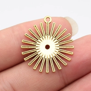 Golden sun ray charm pendant in zinc alloy finish held by fingers on white background