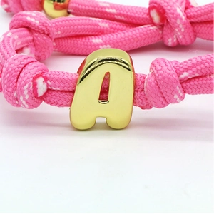 Macro shot of pink woven cord bracelet with polished gold-plated letter A pendant