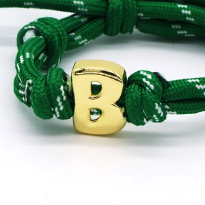 Macro shot of green woven rope bracelet featuring a polished gold metal letter B pendant