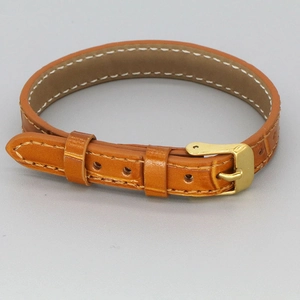 Brown crocodile leather bracelet with golden buckle and white stitching on gray background