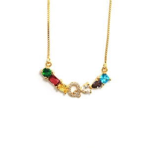 Primer plano detallado de un colgante letra Q dorado con piedras preciosas de varios colores